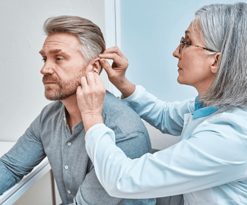 A middle-aged main receiving a hearing aid fitting from an audiologist